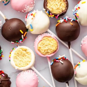 Colorful assortment of cake pops with sprinkles and white chocolate drizzle on marble background.
