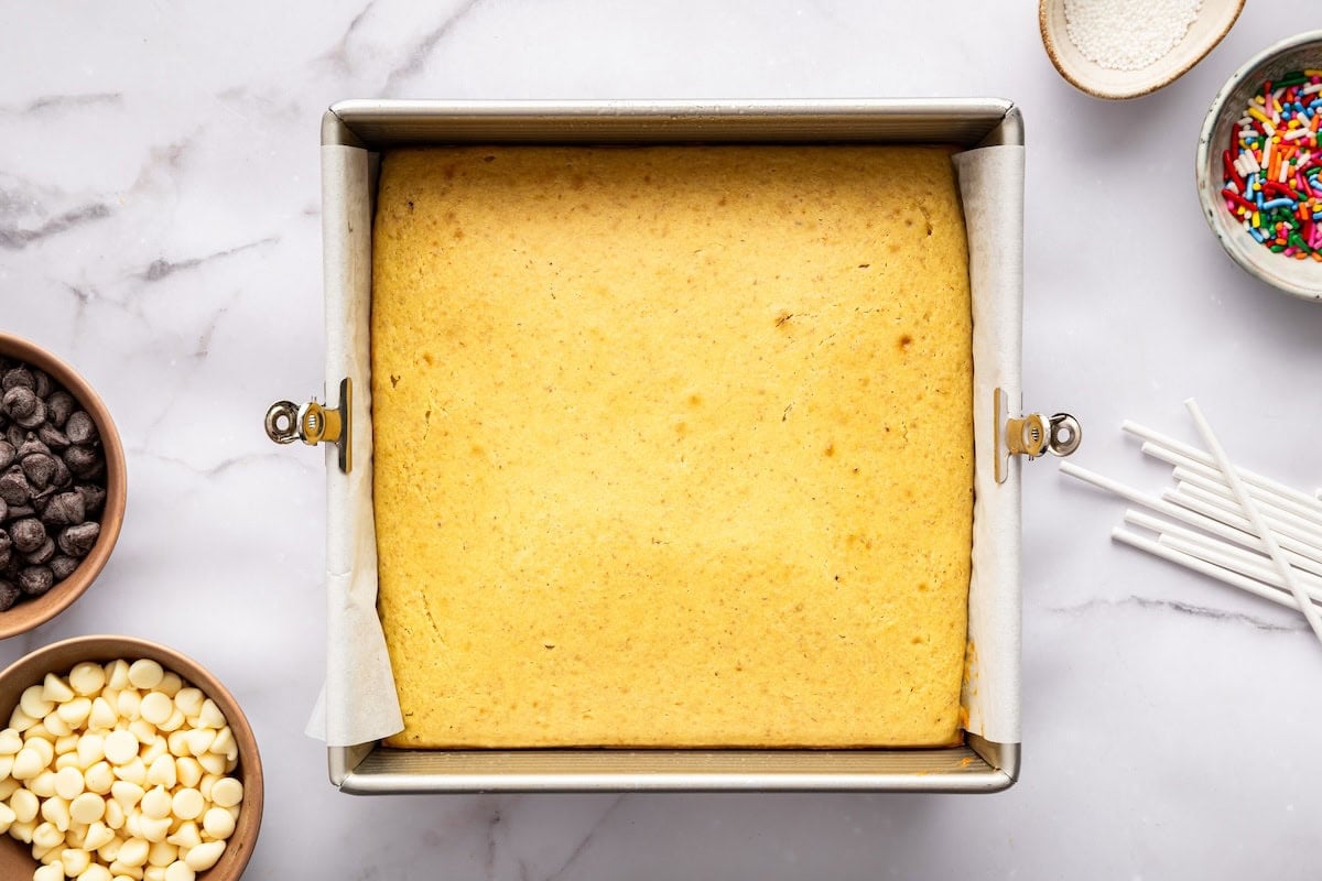 Baked golden cake cooling in a square pan on marble surface.