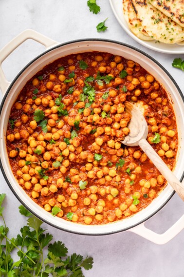 Chickpeas simmering in spiced tomato sauce in a large pot of chana masala.