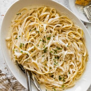 Serving bowl of cottage cheese Alfredo fettuccine topped with parmesan, parsley, and black pepper.