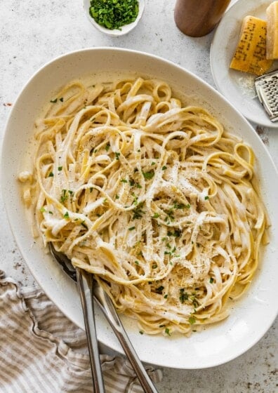 Serving bowl of cottage cheese Alfredo fettuccine topped with parmesan, parsley, and black pepper.