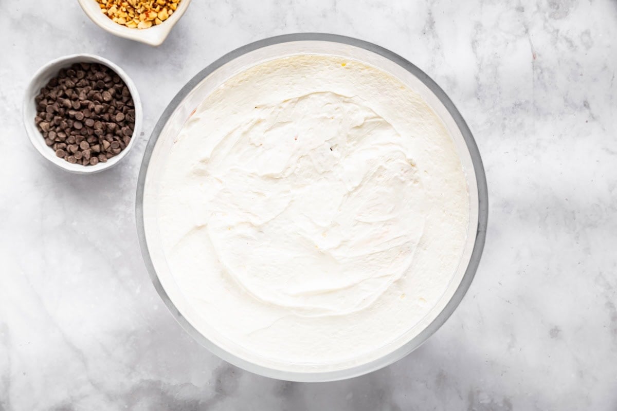 Freshly spread whipped topping layer in a glass bowl for assembling the chocolate trifle.