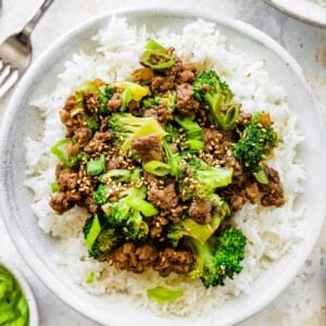 Ground beef and broccoli served on a bed of white rice, topped with sesame seeds and green onions.