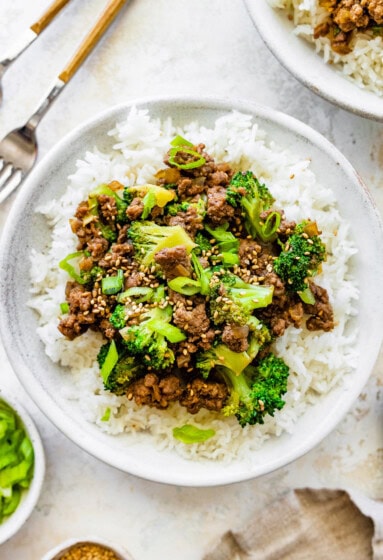 Ground beef and broccoli served on a bed of white rice, topped with sesame seeds and green onions.