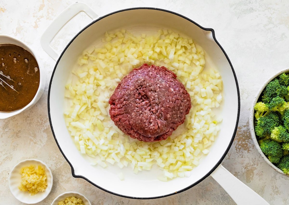 Ground beef being cooked in a skillet with diced onion.