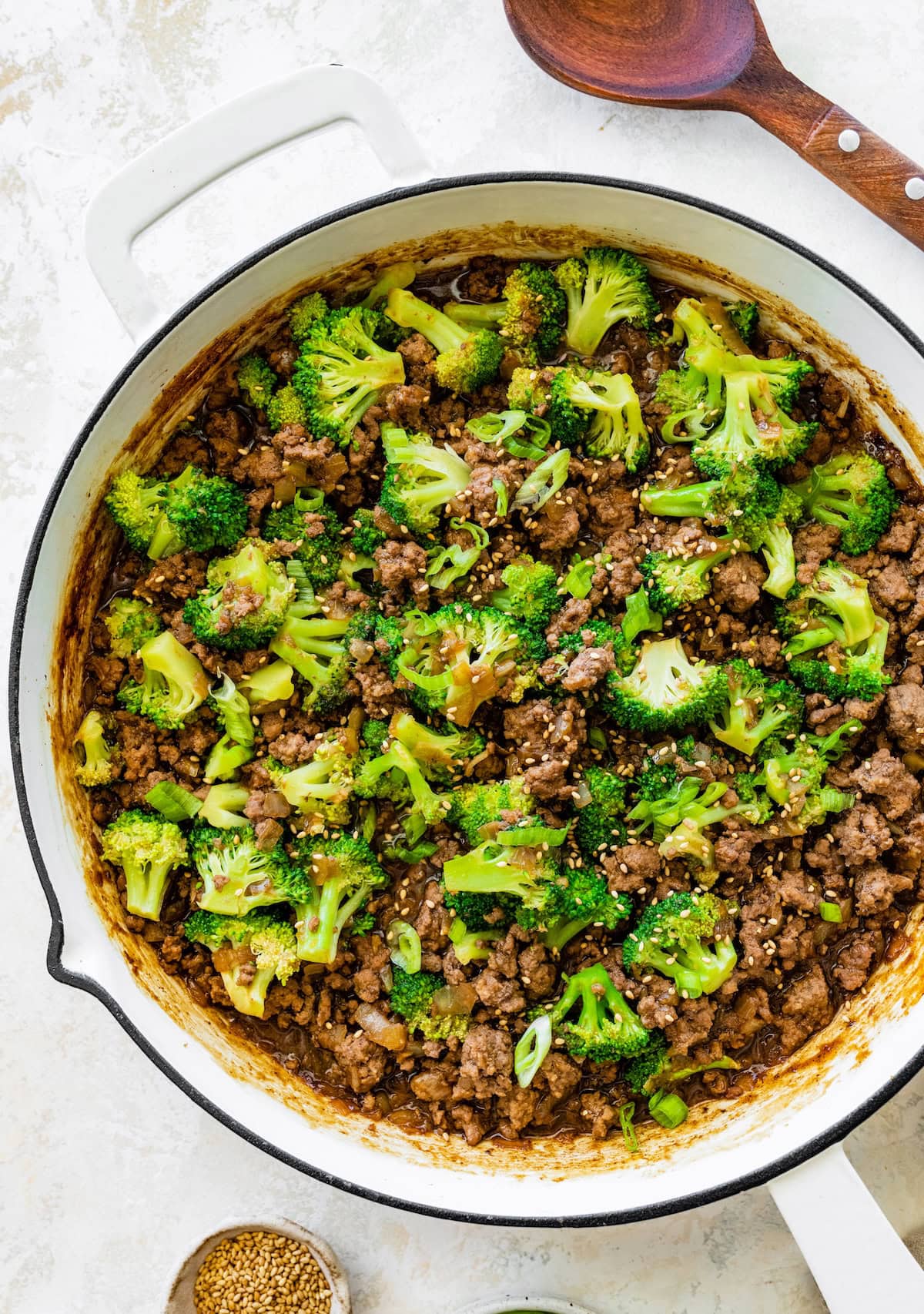 Ground beef and broccoli in a skillet topped with sesame seeds and green onions.