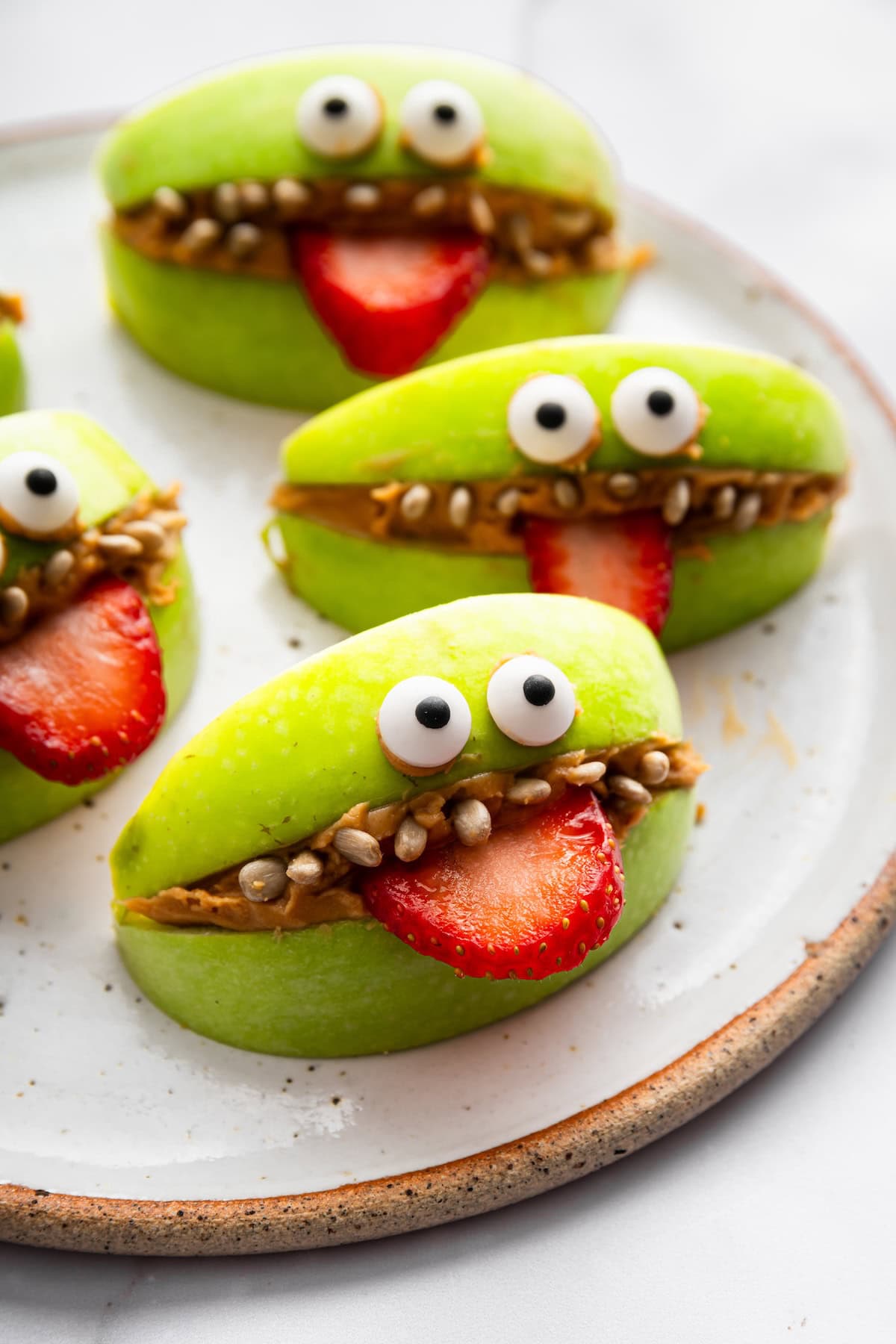 Green apple slices filled with peanut butter, sunflower seed “teeth,” strawberry “tongues,” and candy eyes.
