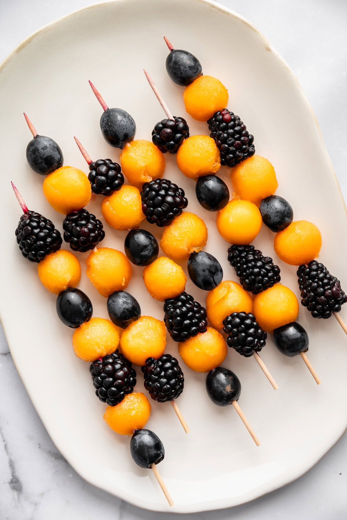 Colorful Halloween fruit skewers with cantaloupe balls, blackberries, and purple grapes in an orange and black pattern.