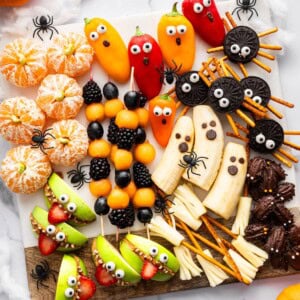 Festive Halloween snack board with banana ghosts, apple monster mouths, clementine pumpkins, Oreo spiders, veggie ghosts, and string cheese broomsticks.