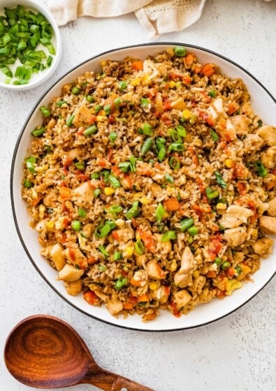 Bowl of homemade chicken fried rice topped with chopped green onions and served on a white table.