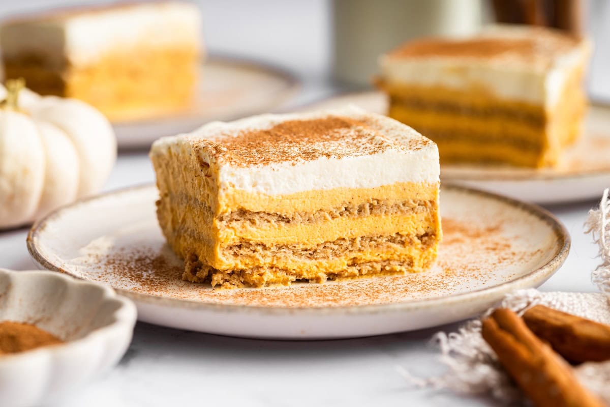 A slice of pumpkin icebox cake on a plate sprinkled with cinnamon, with additional slices in the background.