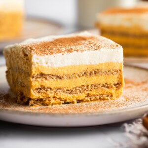 A slice of pumpkin icebox cake on a plate sprinkled with cinnamon, with additional slices in the background.