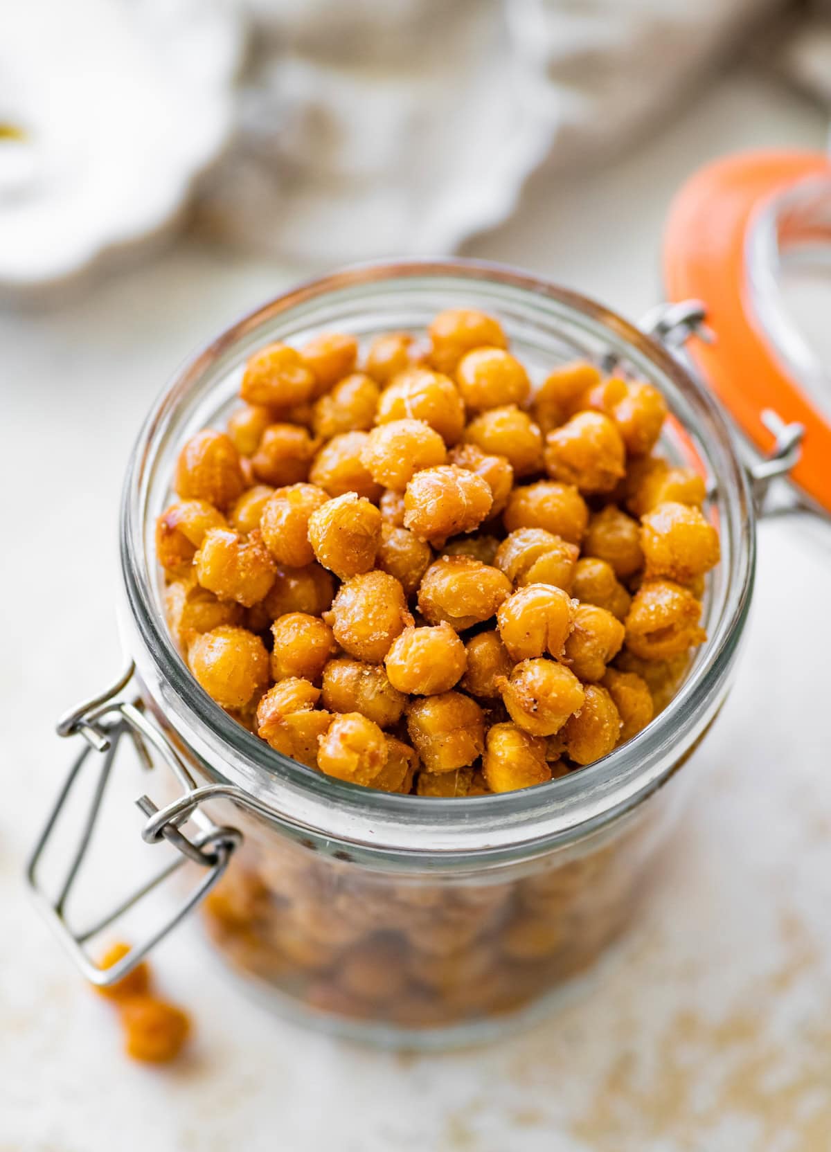 Glass jar of crispy roasted chickpeas next to a few scattered on the counter.