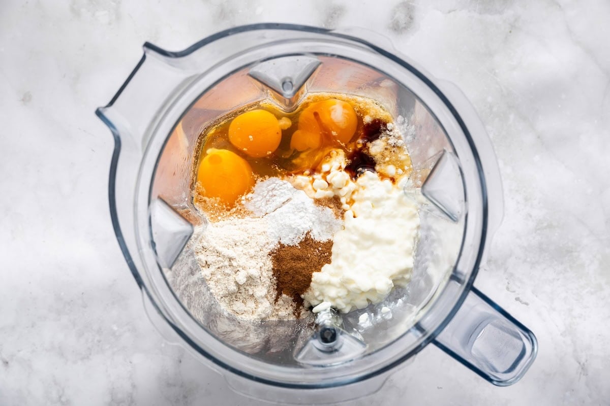 Ingredients for blueberry cottage cheese breakfast bake in a blender, including cottage cheese, eggs, and oat flour.