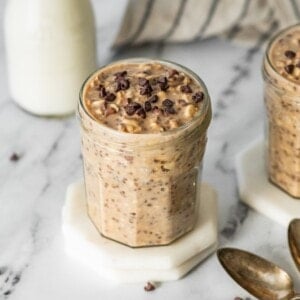 Single jar of cookie dough overnight oats topped with chocolate chips on a white coaster.