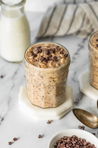 Single jar of cookie dough overnight oats topped with chocolate chips on a white coaster.