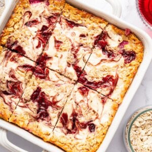 Cottage cheese baked oatmeal in a white baking dish showing creamy cottage cheese and raspberry jam swirls on top.