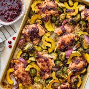 Cranberry balsamic chicken thighs with roasted Brussels sprouts and delicata squash on a sheet pan.