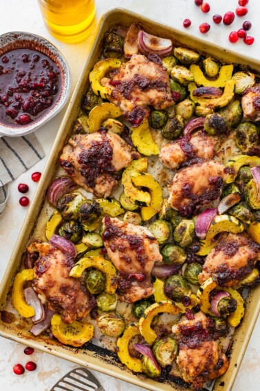 Cranberry balsamic chicken thighs with roasted Brussels sprouts and delicata squash on a sheet pan.