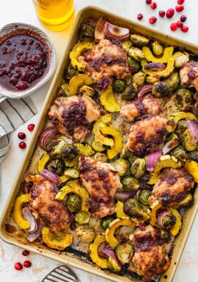 Cranberry balsamic chicken thighs with roasted Brussels sprouts and delicata squash on a sheet pan.