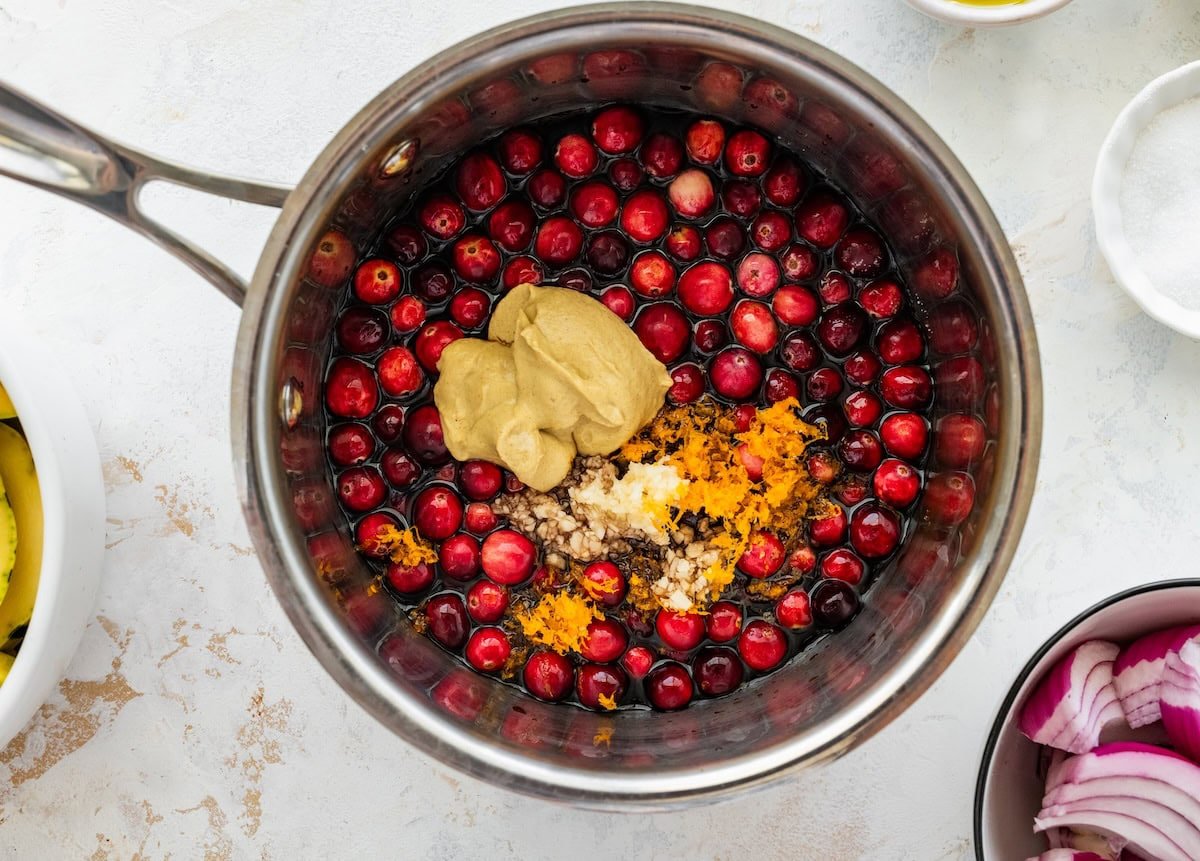 Cranberries, Dijon mustard, garlic, and orange zest simmering together in a small saucepan.