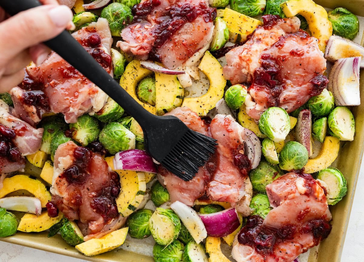 Chicken thighs brushed with cranberry balsamic glaze surrounded by Brussels sprouts and squash before roasting.