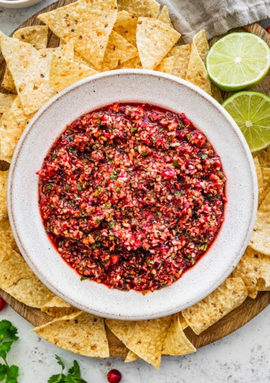 Fresh cranberry salsa served in a white bowl on a wooden tray surrounded by tortilla chips for serving.