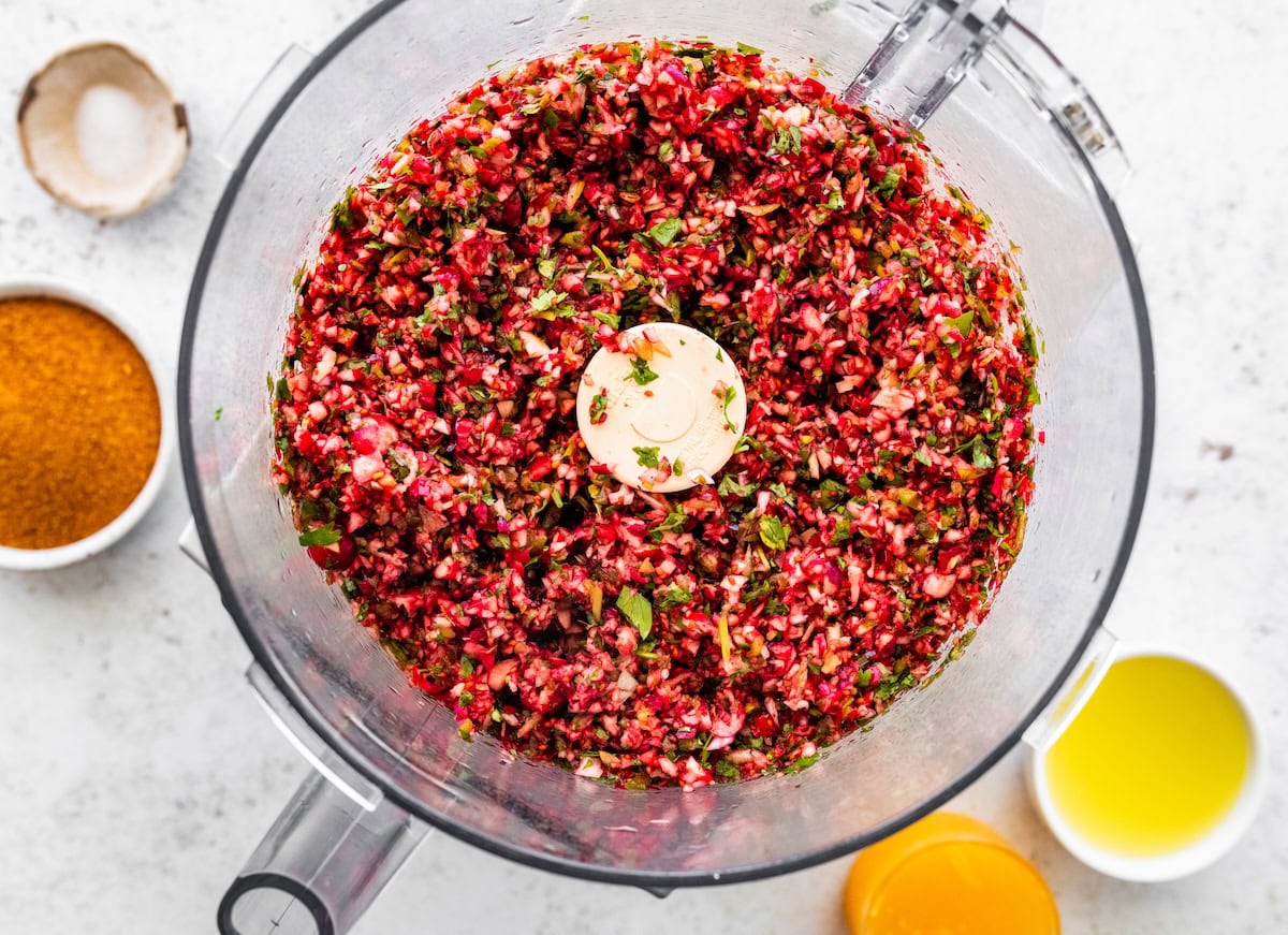 Cranberry salsa ingredients pulsed together in a food processor, showing a chunky, colorful texture.