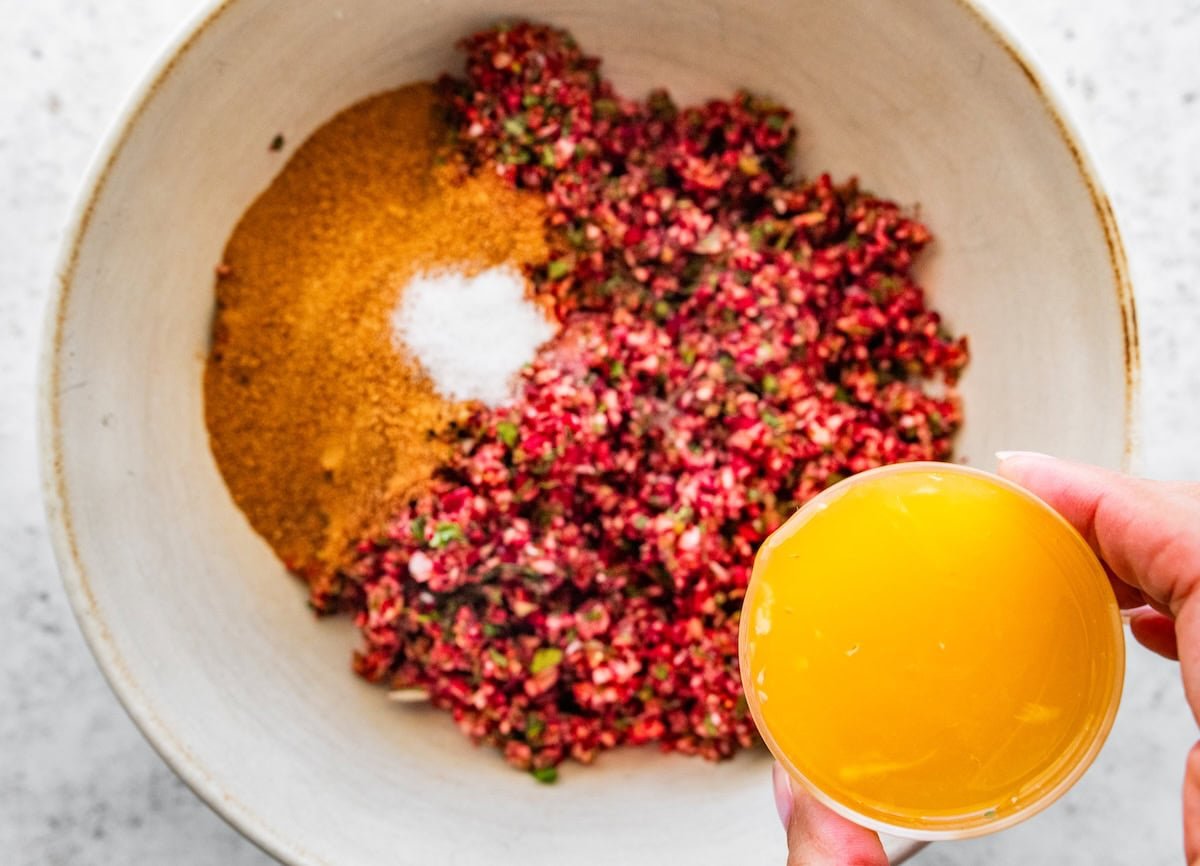 Pouring fresh orange juice into a bowl of chopped cranberry salsa mixture.