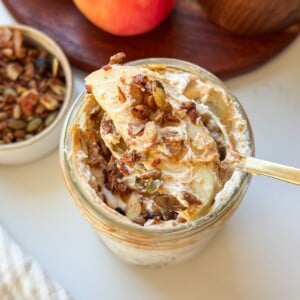 A spoonful of high protein apple salad with an apple slice and granola, held over a mason jar.