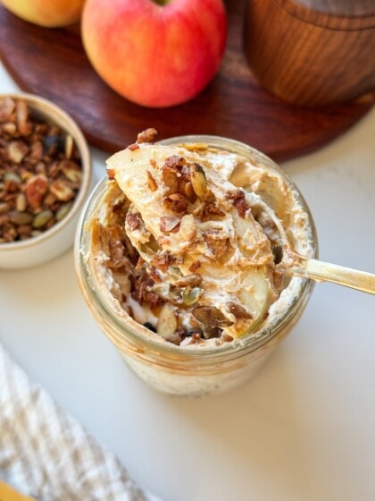 A spoonful of high protein apple salad with an apple slice and granola, held over a mason jar.