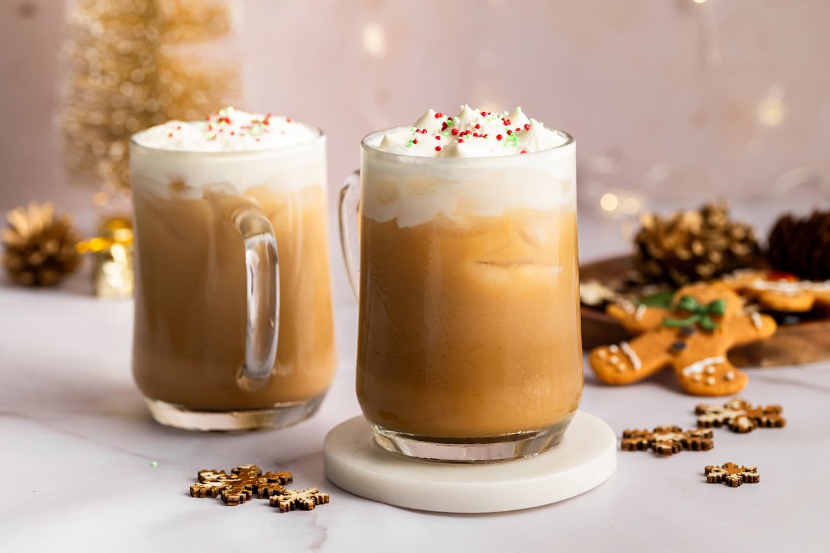 Two iced sugar cookie lattes topped with whipped cream and sprinkles on a holiday-themed table.