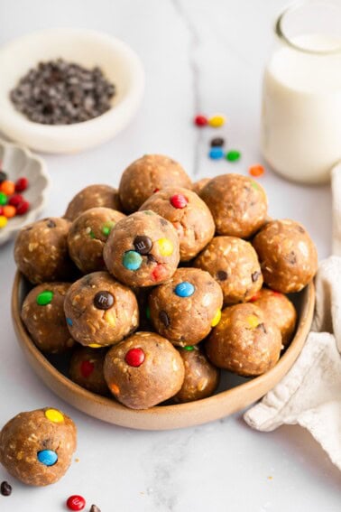 Monster cookie protein balls stacked in a bowl with colorful M&M’s and mini chocolate chips.