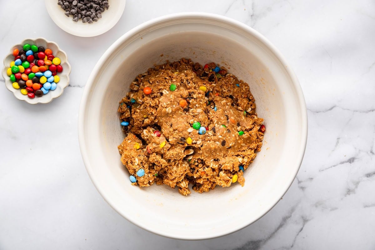 Monster cookie protein ball dough mixed in a bowl with oats, chocolate chips, and M&M&rsquo;s.