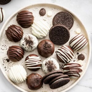 Assorted Oreo balls coated in dark and white chocolate on a serving plate alongside a few Oreo cookies.