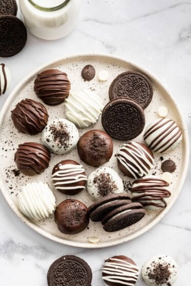 Assorted Oreo balls coated in dark and white chocolate on a serving plate alongside a few Oreo cookies.