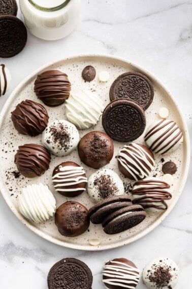 Assorted Oreo balls coated in dark and white chocolate on a serving plate alongside a few Oreo cookies.