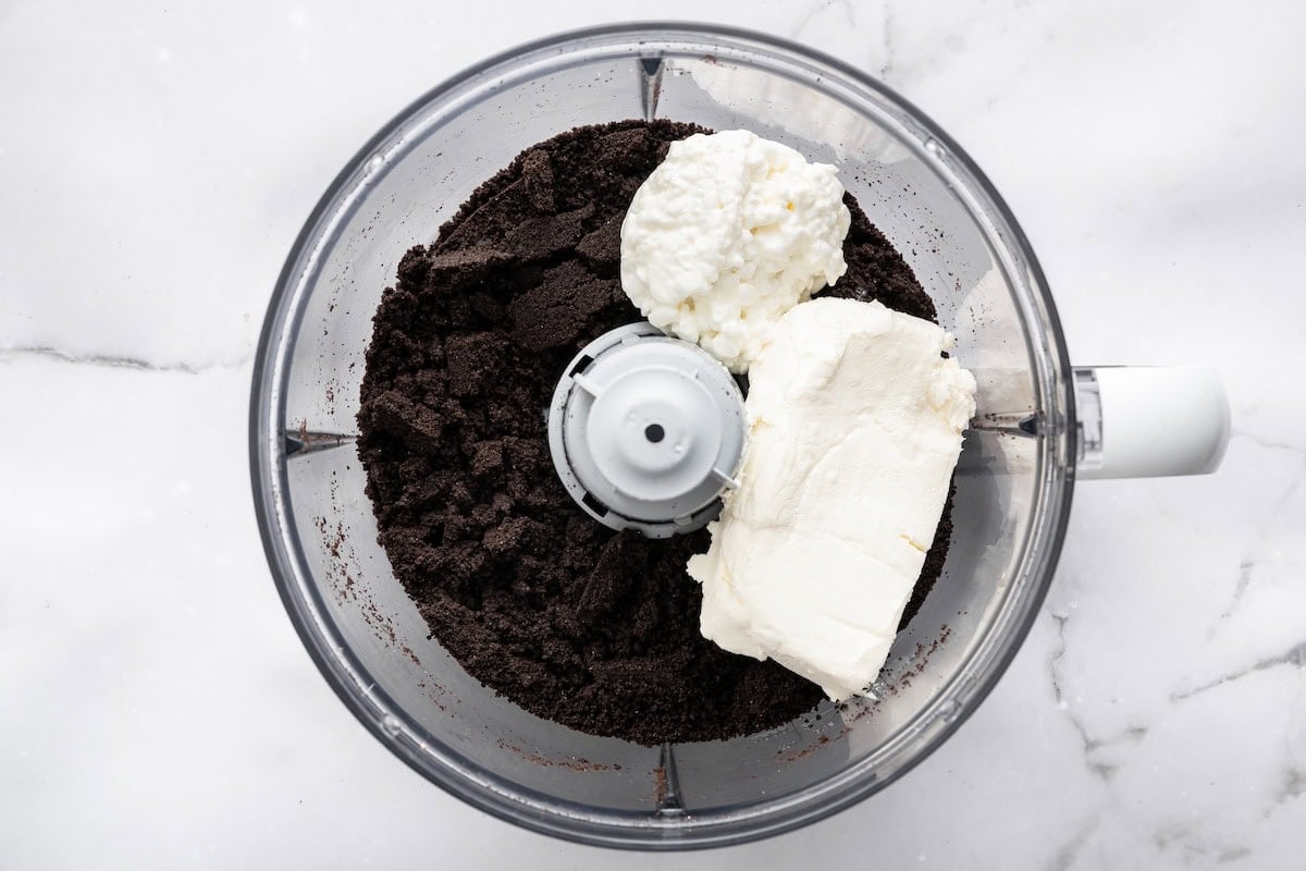Food processor filled with Oreo crumbs, cream cheese and cottage cheese before blending.
