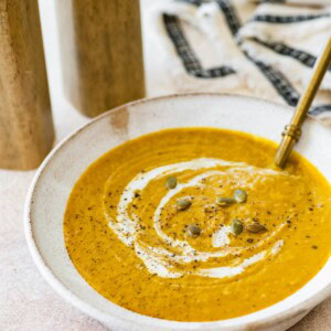 Pumpkin curry soup in a white serving bowl, topped with a coconut milk swirl, black pepper, and pumpkin seeds.