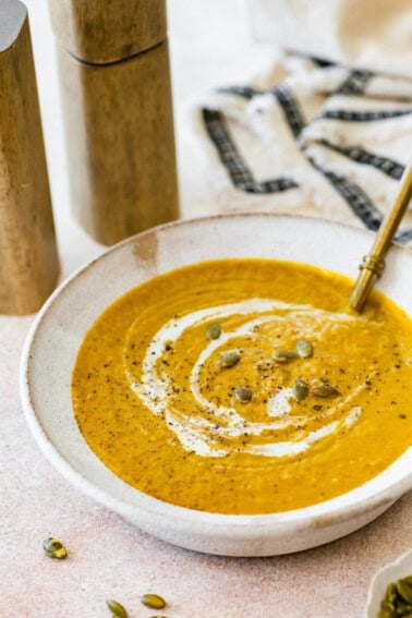 Pumpkin curry soup in a white serving bowl, topped with a coconut milk swirl, black pepper, and pumpkin seeds.
