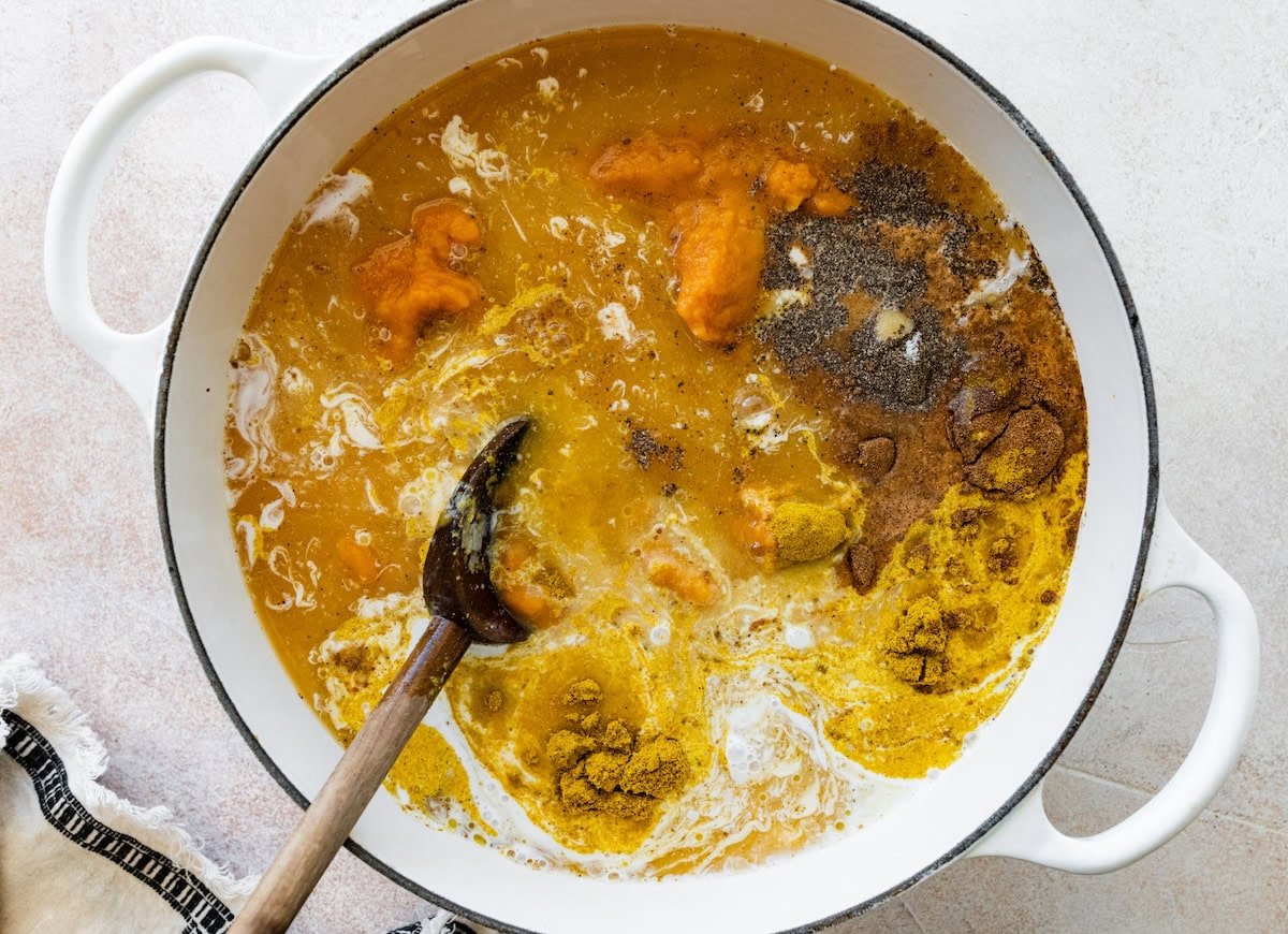 Pumpkin curry soup in a large pot with a wooden serving spoon.