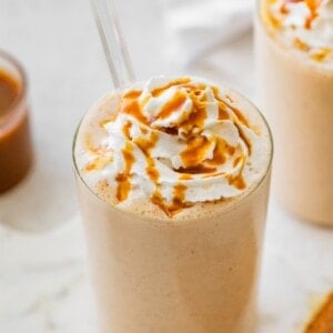 Salted caramel protein shake topped with whipped cream and caramel drizzle served with a straw.