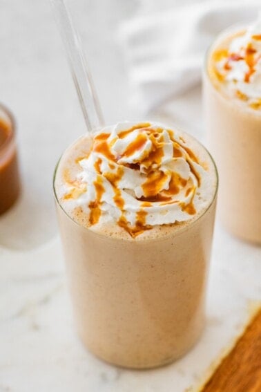 Salted caramel protein shake topped with whipped cream and caramel drizzle served with a straw.