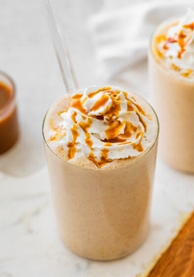Salted caramel protein shake topped with whipped cream and caramel drizzle served with a straw.