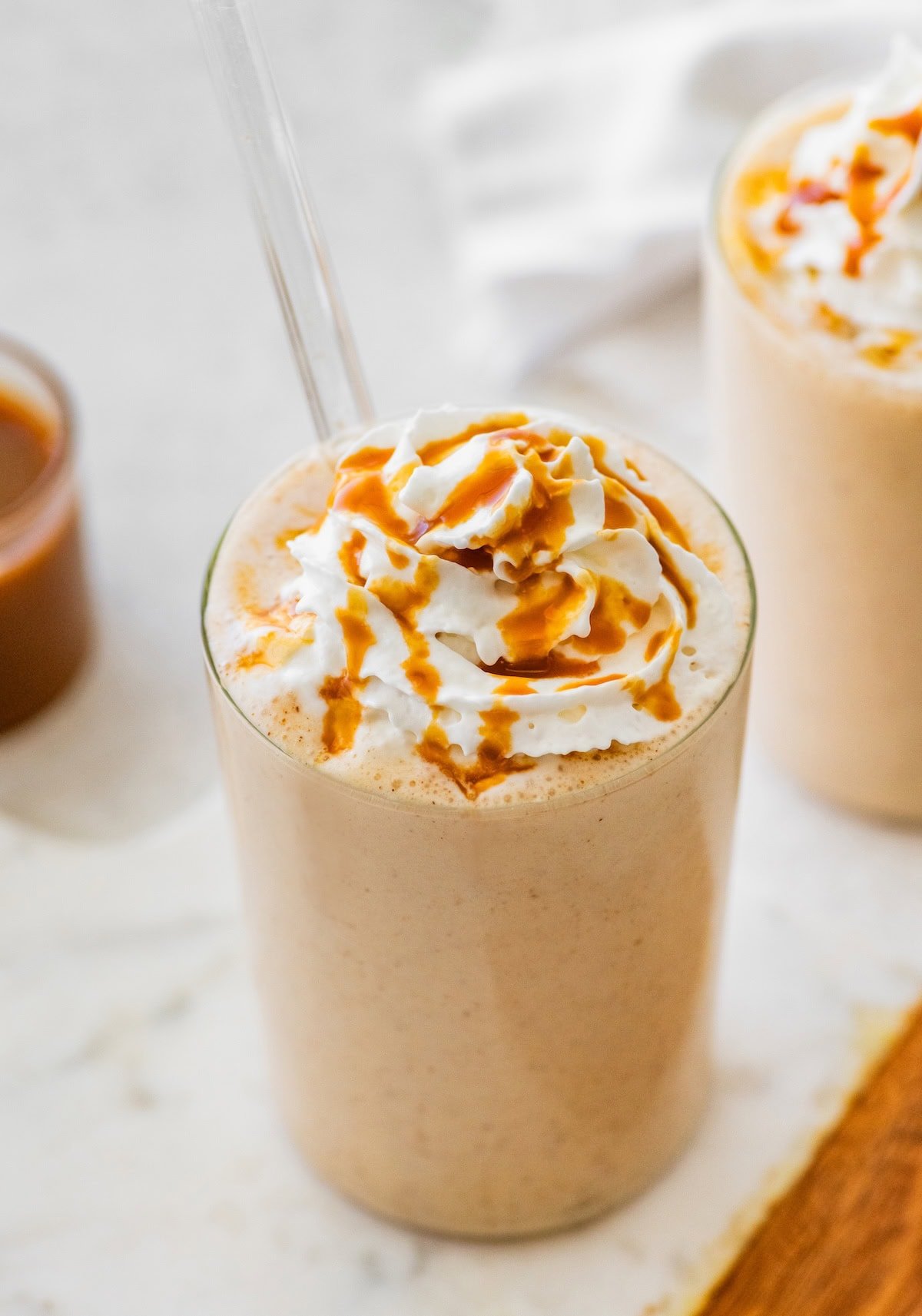 Salted caramel protein shake topped with whipped cream and caramel drizzle served with a straw.