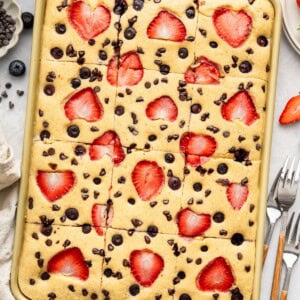Sheet pan pancakes topped with strawberries and chocolate chips, freshly baked and cut into squares.