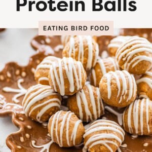 Gingerbread protein balls drizzled with white chocolate stacked on a decorative plate