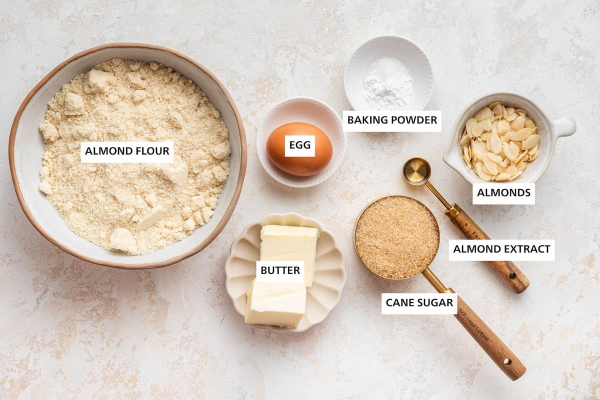 Ingredients measured out to make Almond Cookies: almond flour, butter, egg, cane sugar, baking powder, almond extract and almonds.