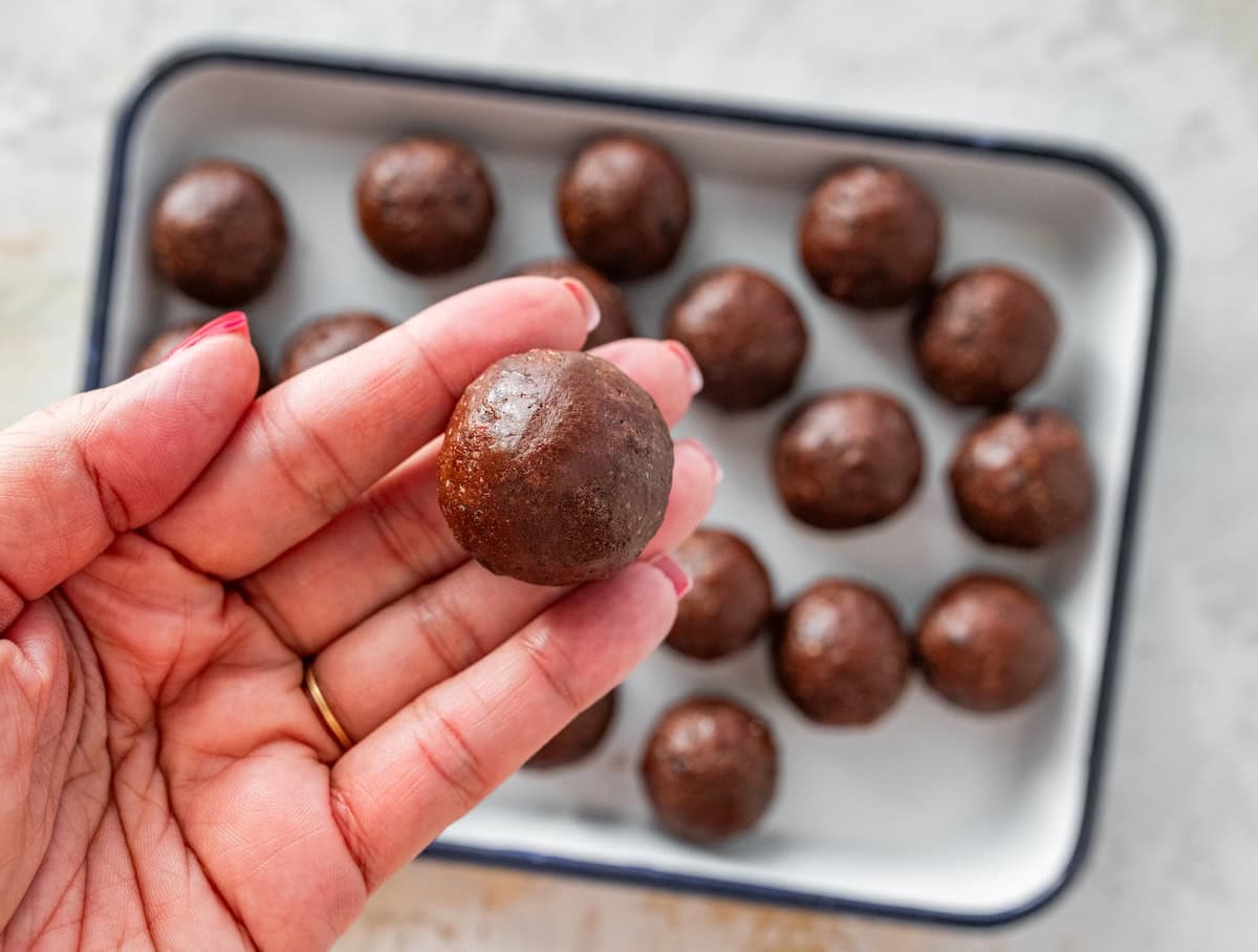 Hand holding a rolled chocolate protein ball over a tray of shaped balls.