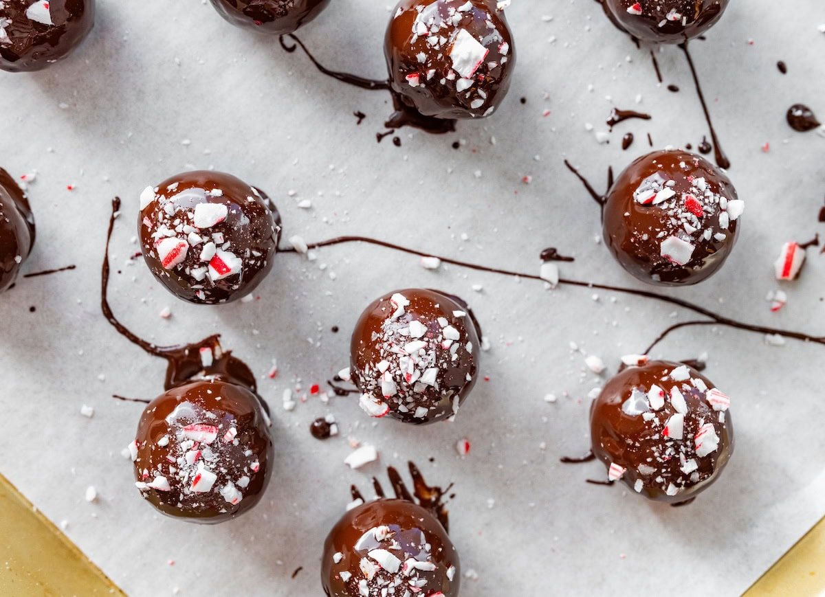 Chocolate peppermint protein balls drying on parchment coated in chocolate and topped with crushed candy canes.
